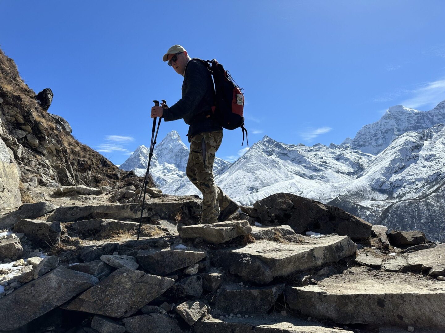 A man with a backpack and hiking poles on top of rocks.