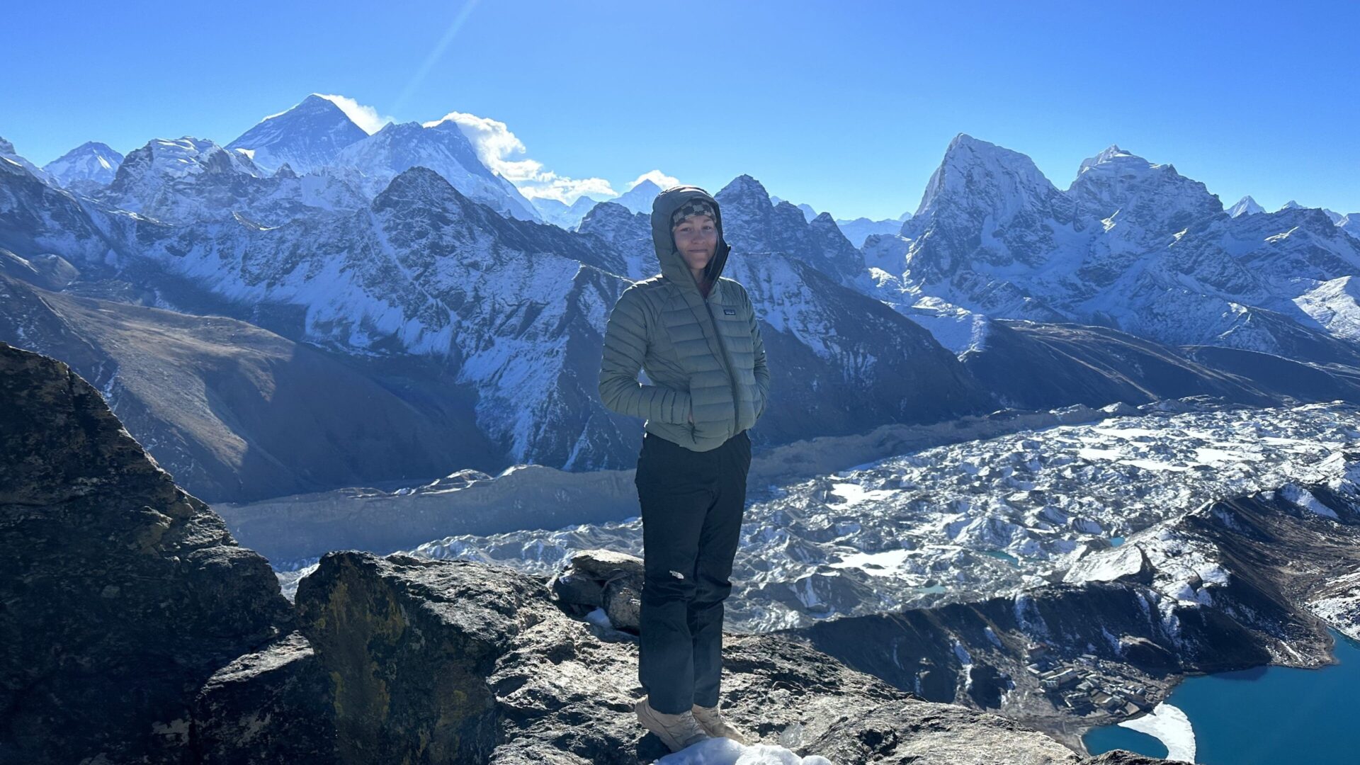 A person standing on top of a mountain with snow covered mountains in the background.