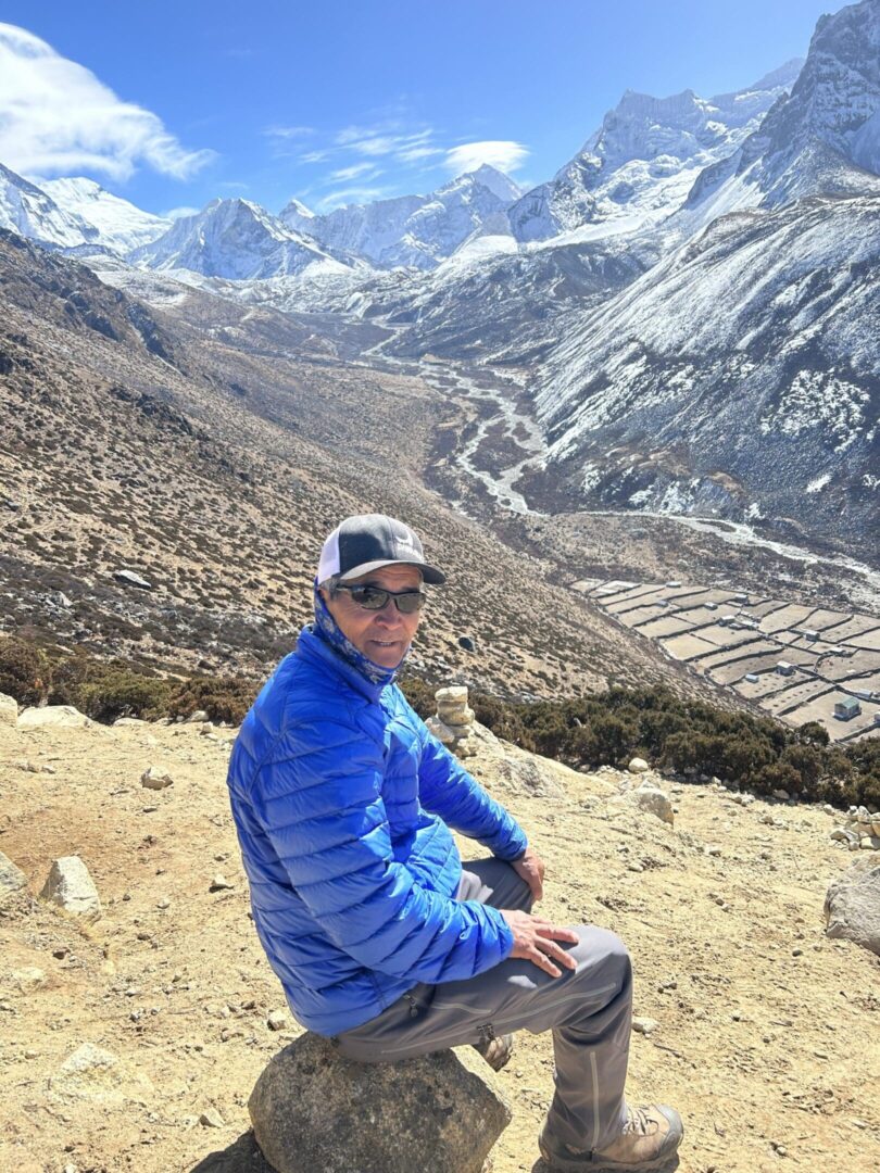 A man sitting on the ground in front of mountains.