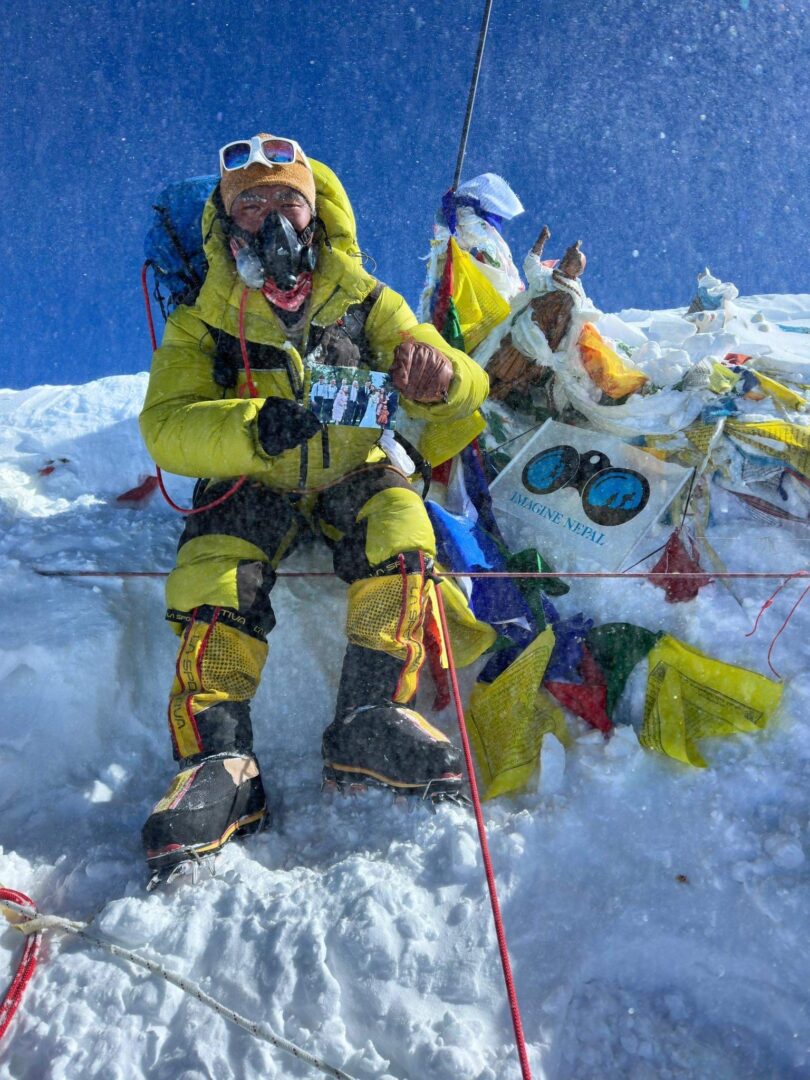 A man in yellow jacket sitting on top of snow covered ground.