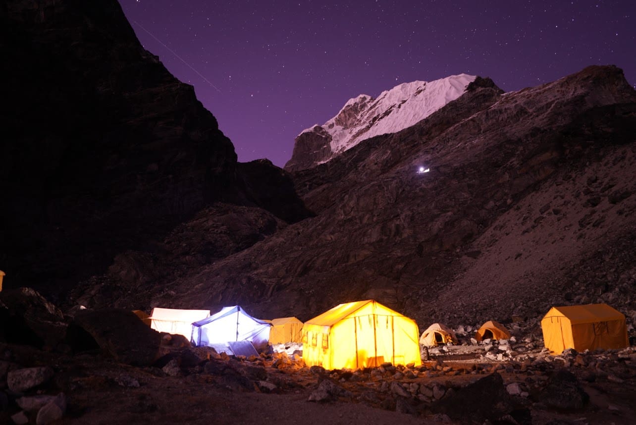 A group of tents lit up at night in the mountains.