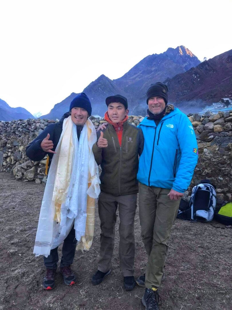 Three people standing in front of a mountain.