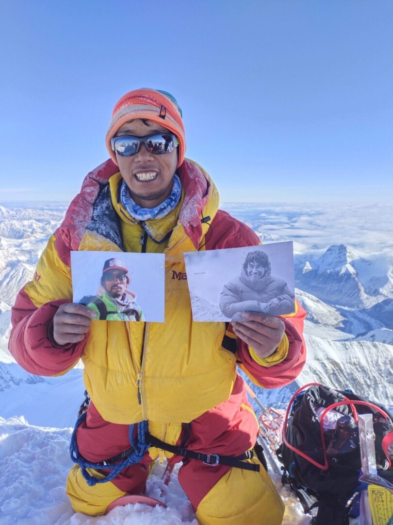 A man holding up two pictures of himself on top of a mountain.