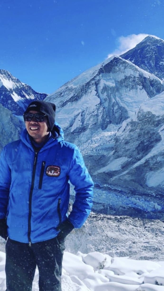 A man in blue jacket standing on top of a mountain.